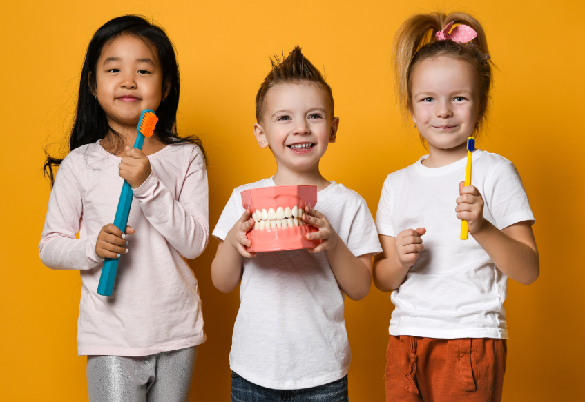 Kids holding toothbrushes and fake teeth, smiling